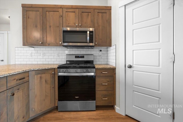 kitchen with decorative backsplash, appliances with stainless steel finishes, wood finished floors, and light stone countertops