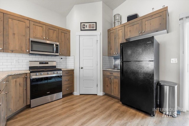 kitchen with appliances with stainless steel finishes, tasteful backsplash, vaulted ceiling, light wood-type flooring, and light stone counters