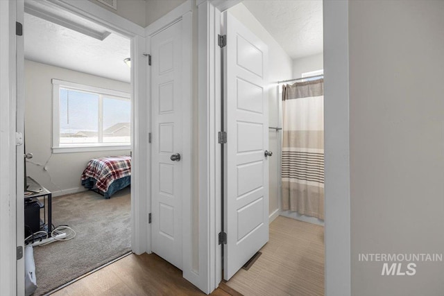 hall featuring baseboards, a textured ceiling, carpet flooring, and wood finished floors