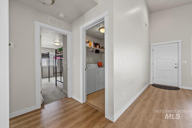 corridor featuring wood finished floors, baseboards, independent washer and dryer, and visible vents