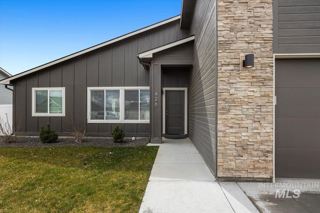 entrance to property featuring board and batten siding, a yard, and stone siding
