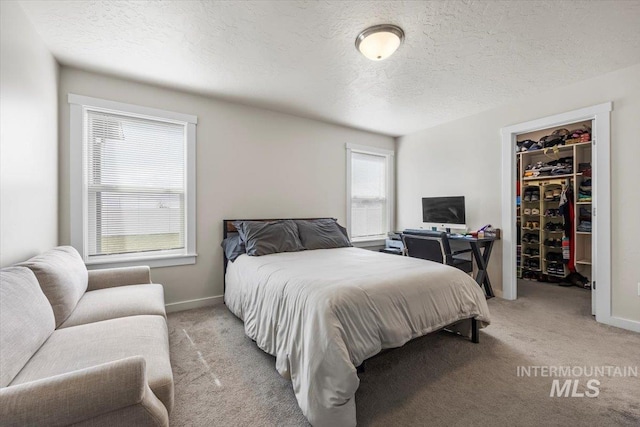 bedroom with light colored carpet, a walk in closet, a textured ceiling, baseboards, and a closet