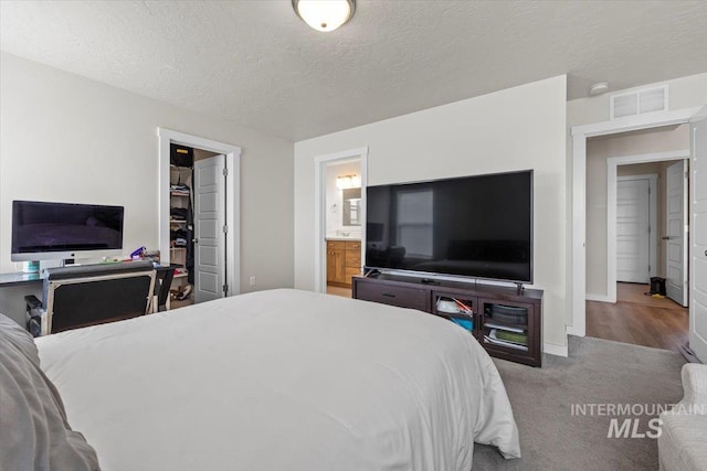 carpeted bedroom featuring connected bathroom, a textured ceiling, visible vents, baseboards, and a spacious closet