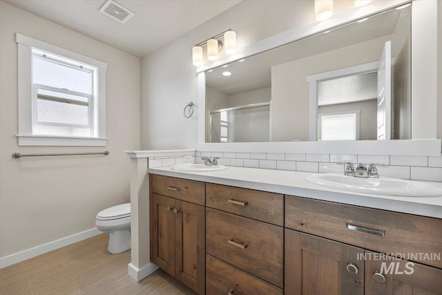 bathroom featuring toilet, baseboards, a sink, and a stall shower