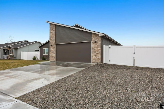 view of front facade featuring fence, an attached garage, stone siding, a gate, and concrete driveway