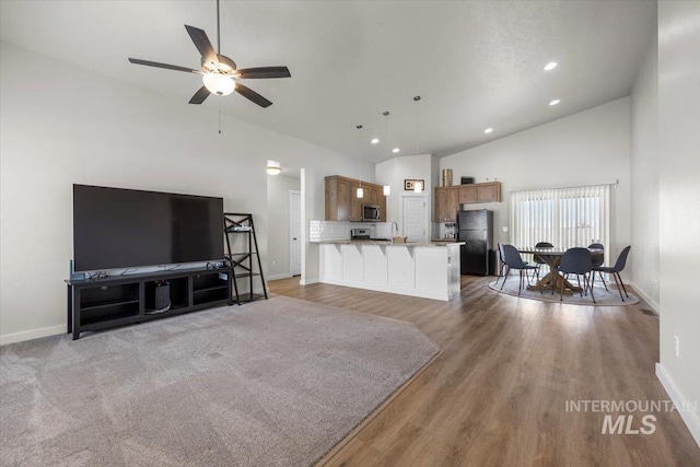 living area with baseboards, ceiling fan, and high vaulted ceiling