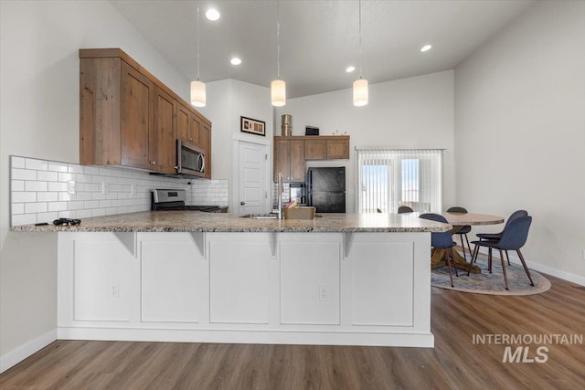kitchen with brown cabinetry, stainless steel appliances, a peninsula, wood finished floors, and tasteful backsplash