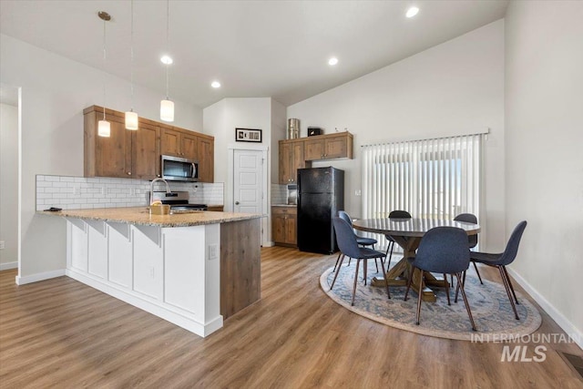 kitchen with appliances with stainless steel finishes, brown cabinetry, a peninsula, baseboards, and decorative backsplash