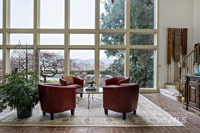 living room with stairway, a high ceiling, brick floor, and a wealth of natural light