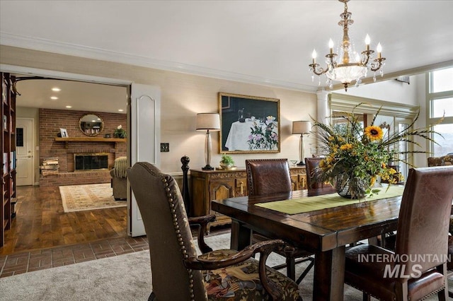 dining room featuring an inviting chandelier, a brick fireplace, brick floor, and ornamental molding