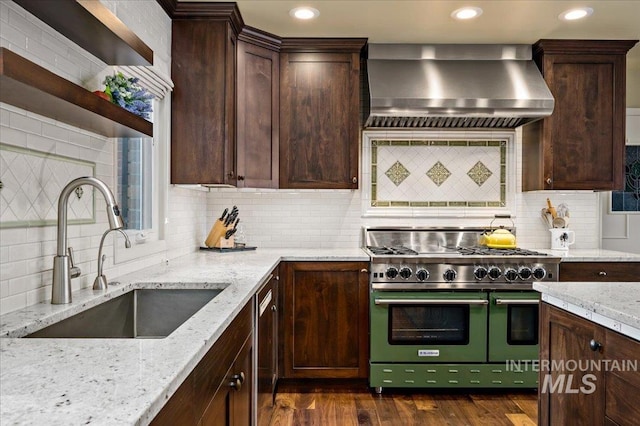 kitchen featuring dark wood-style floors, a sink, stainless steel appliances, dark brown cabinets, and wall chimney exhaust hood