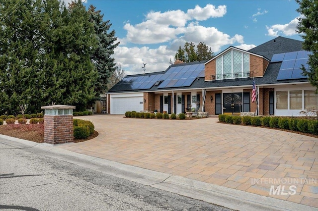 view of front of house featuring decorative driveway, brick siding, roof mounted solar panels, and a chimney