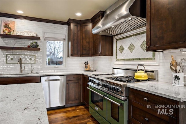 kitchen featuring dark wood-style floors, a sink, stainless steel appliances, dark brown cabinetry, and wall chimney exhaust hood