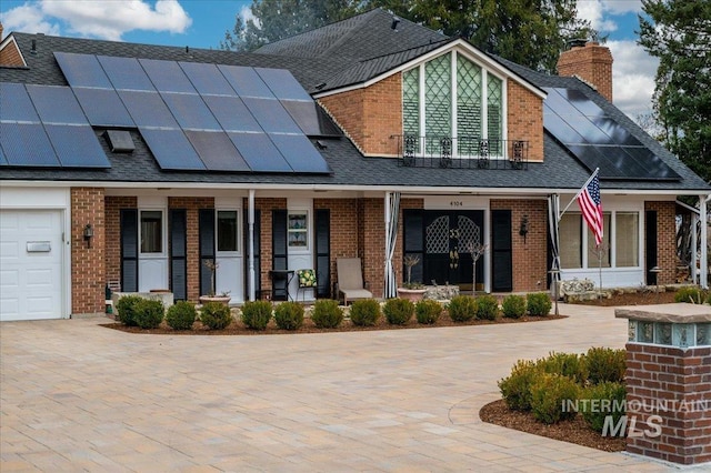 view of front facade with brick siding, covered porch, roof mounted solar panels, and a shingled roof