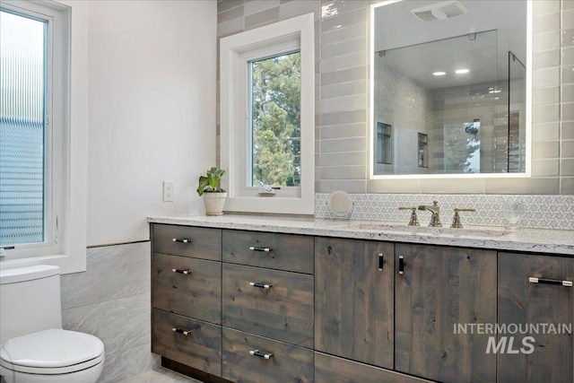 bathroom featuring vanity, visible vents, a shower stall, tile walls, and toilet