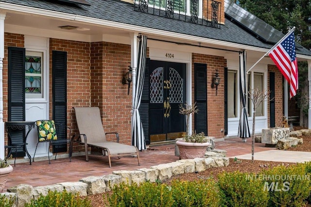 property entrance with brick siding, a porch, solar panels, and a shingled roof