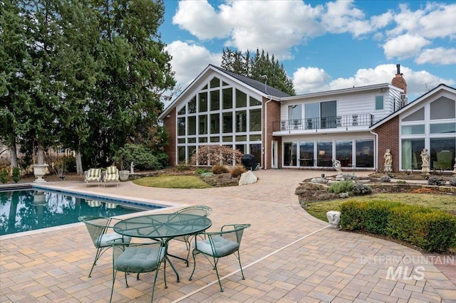 back of property with brick siding, a chimney, a balcony, an outdoor pool, and a patio