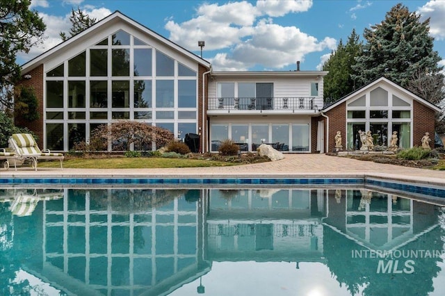 rear view of house with an outdoor pool, a balcony, and a patio area