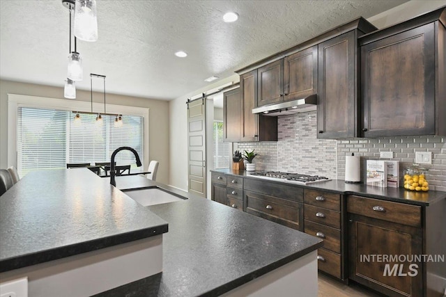 5988 N Lichfield Ave, Meridian, ID 83646 - kitchen featuring stainless steel gas cooktop, dark brown cabinetry, dark countertops, under cabinet range hood, and a sink