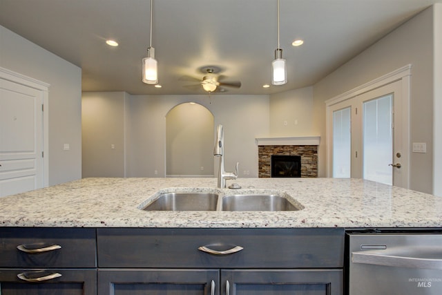 kitchen featuring light stone countertops, ceiling fan, a sink, dishwasher, and open floor plan