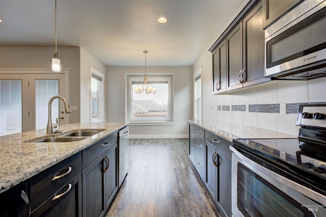 kitchen featuring a sink, light stone counters, backsplash, appliances with stainless steel finishes, and a chandelier