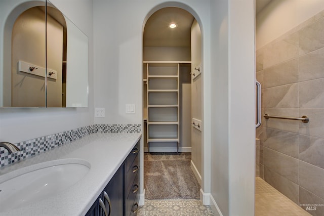 bathroom featuring a tile shower, vanity, a walk in closet, and baseboards