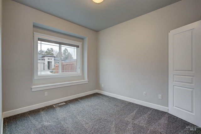 empty room with visible vents, dark carpet, and baseboards