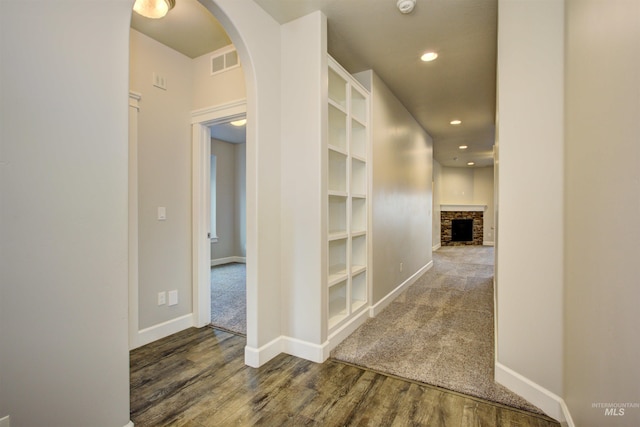 hallway featuring wood finished floors, arched walkways, visible vents, and baseboards