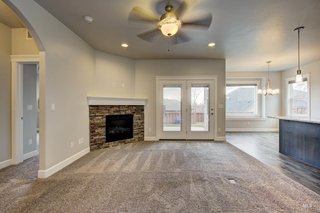 unfurnished living room with baseboards, recessed lighting, arched walkways, a stone fireplace, and ceiling fan with notable chandelier