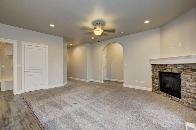 unfurnished living room with a ceiling fan, recessed lighting, arched walkways, a fireplace, and baseboards