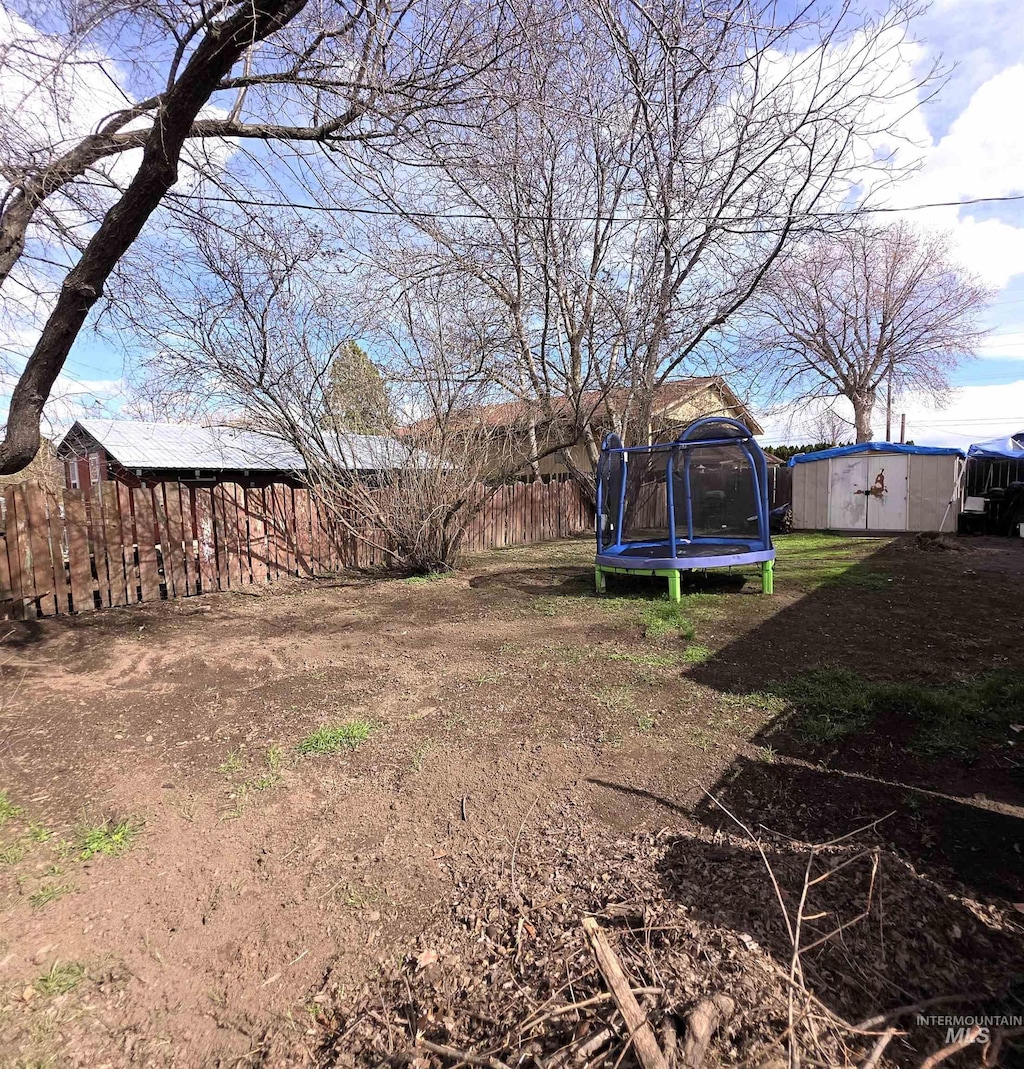 view of yard featuring an outbuilding, a shed, a trampoline, and fence