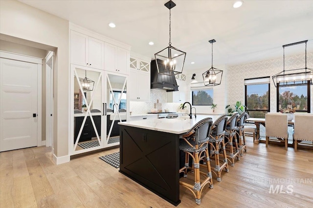 965 S Ranch House Way, Eagle, ID 83616 - kitchen featuring custom exhaust hood, white cabinetry, light wood finished floors, a kitchen island with sink, and a chandelier