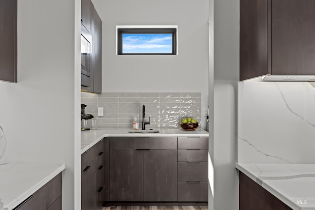 kitchen featuring light stone counters, a sink, a wealth of natural light, and decorative backsplash