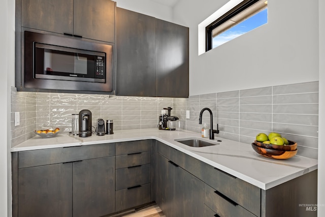 kitchen featuring dark brown cabinets, decorative backsplash, a sink, and built in microwave