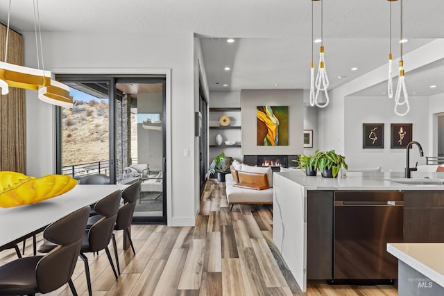 kitchen featuring pendant lighting, light countertops, stainless steel dishwasher, a glass covered fireplace, and a sink