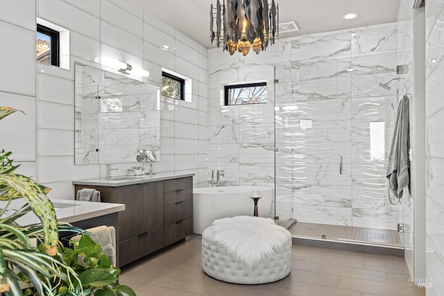 full bath featuring tile walls, visible vents, a freestanding bath, a stall shower, and vanity