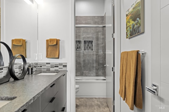 full bath with double vanity, toilet, shower / bath combination with glass door, a sink, and backsplash