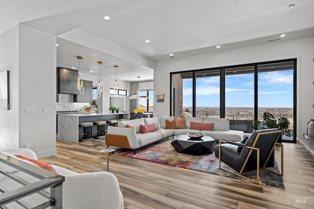 living area featuring light wood-style floors, a healthy amount of sunlight, visible vents, and a textured ceiling