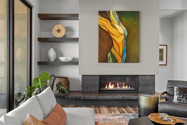 living area with wood finished floors, a glass covered fireplace, visible vents, and built in features