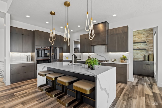 kitchen with built in appliances, a sink, hanging light fixtures, an island with sink, and modern cabinets