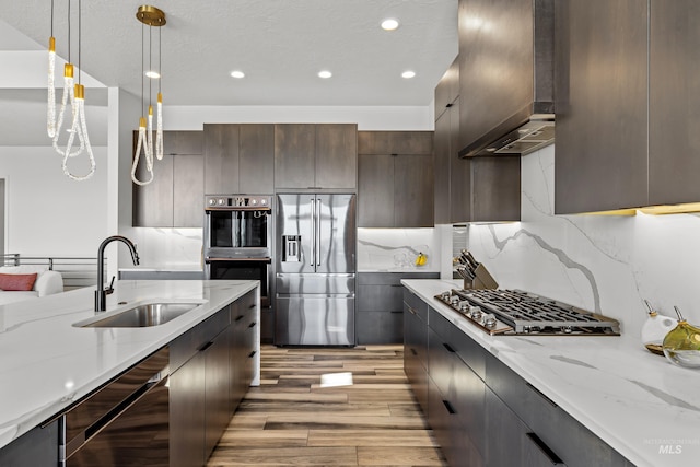 kitchen featuring modern cabinets, appliances with stainless steel finishes, hanging light fixtures, wall chimney range hood, and a sink