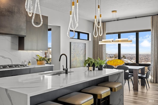 kitchen featuring decorative backsplash, modern cabinets, decorative light fixtures, light wood-style floors, and a sink