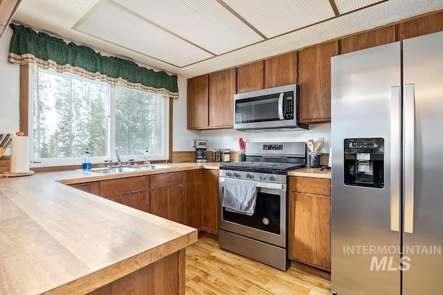 kitchen featuring a sink, stainless steel appliances, brown cabinetry, and light countertops