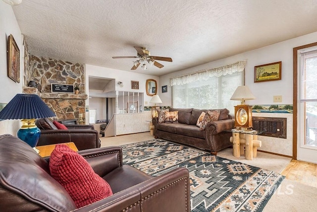 carpeted living room with a stone fireplace, a textured ceiling, and a ceiling fan