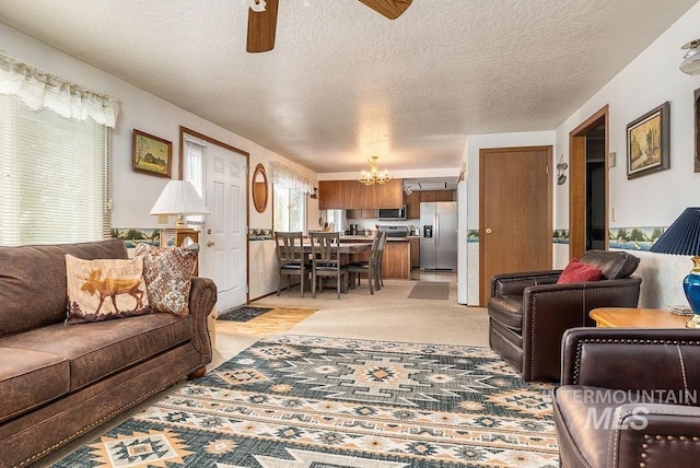 living room featuring ceiling fan with notable chandelier, light colored carpet, and a textured ceiling