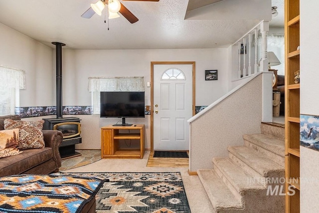 carpeted living room featuring stairway, a ceiling fan, a wood stove, and a textured ceiling