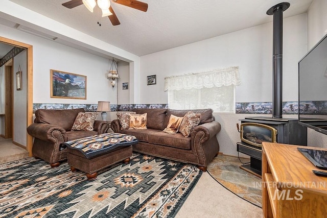 living room featuring a wood stove, ceiling fan, and carpet floors