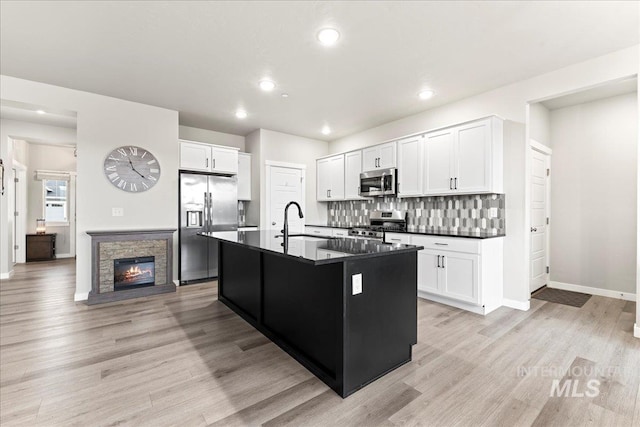 kitchen with light wood-type flooring, decorative backsplash, dark countertops, and appliances with stainless steel finishes