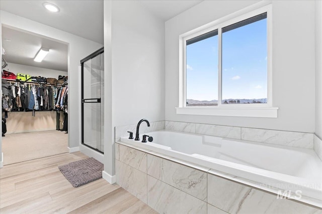 bathroom with a garden tub, a shower stall, wood finished floors, and a spacious closet