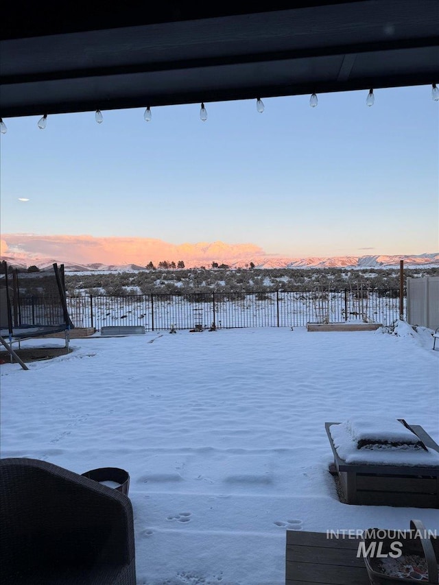 yard layered in snow featuring a trampoline and fence